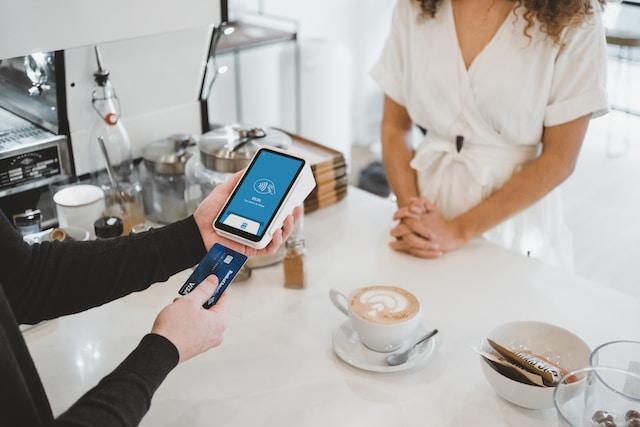 A patron at a cafe, about to insert a chip credit card into a mobile payment terminal