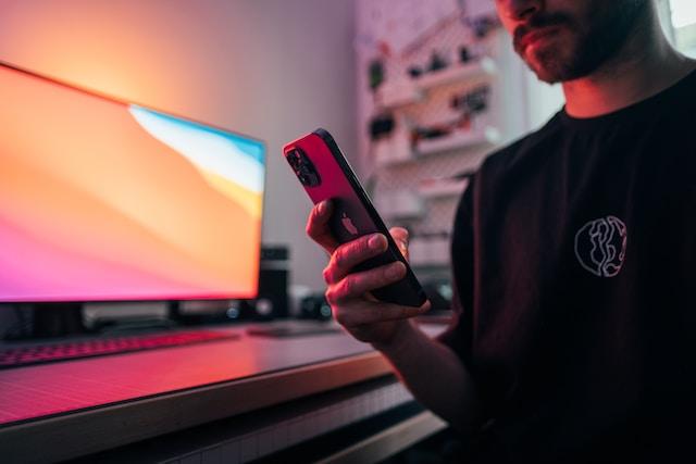 A man in front of a computer, looking at his mobile phone