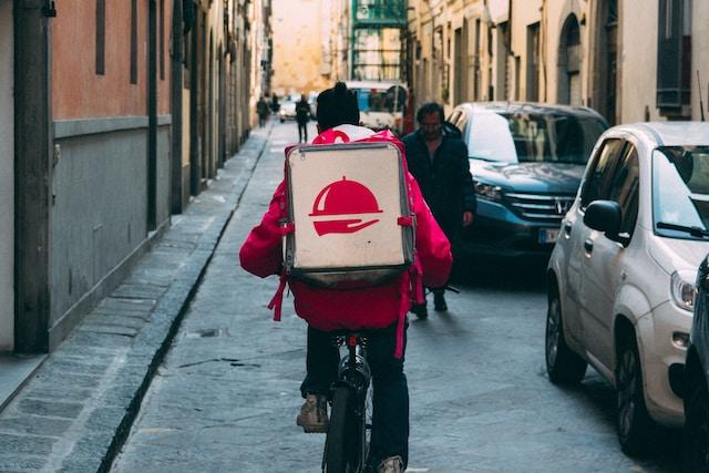 A delivery worker con a bicycle seen from the back, carrying a food order